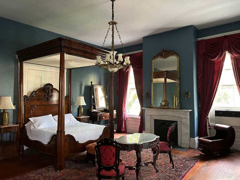 The Little Kingdom: a beautiful dark blue room with a queen size full tester bed signed by C. Lee. This room has an adjoining sitting room (the game room) overlooking the bayou as well as a large marble tiled bathroom with soaking tub and 60-inch marble top vanity. The name refers to the fact that the name Albania is said to translate to “Little Kingdom” in English.